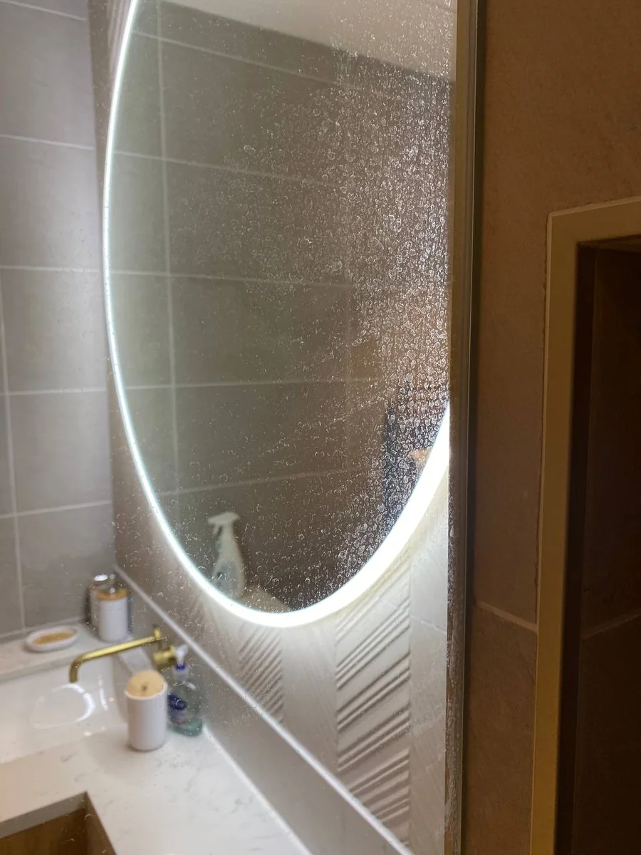 Round LED bathroom mirror covered in water spots and limescale before cleaning