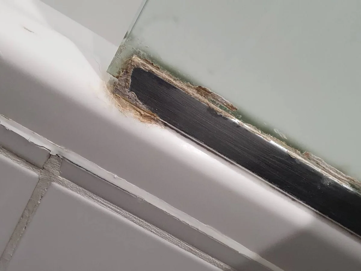 Shower screen trim and bath edge with limescale and mould before cleaning