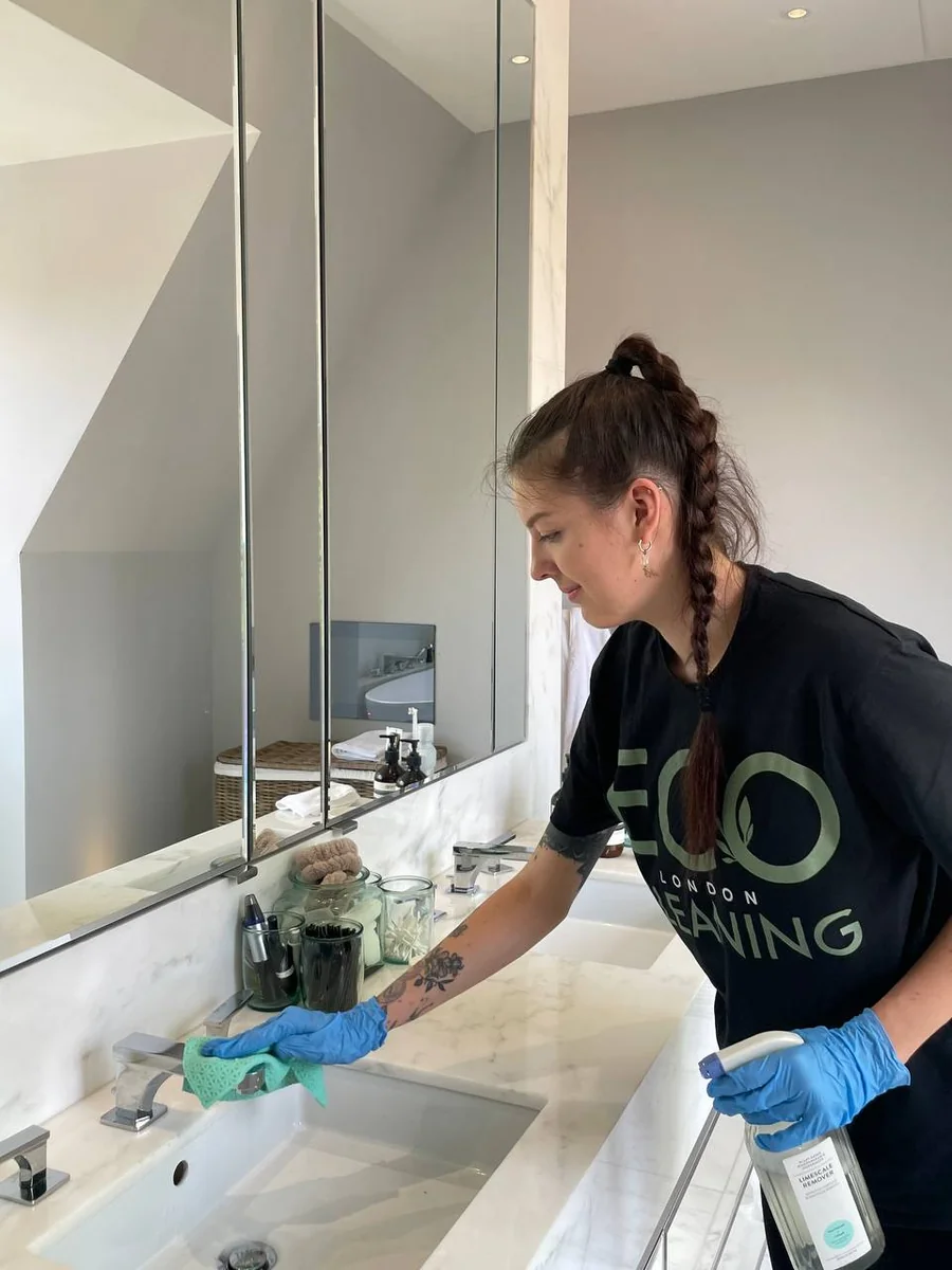 Cleaner wiping a bathroom sink with eco-friendly spray during a regular clean